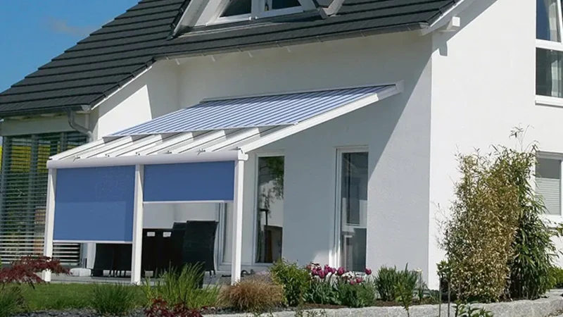 Moderne Terrassenüberdachung mit blauen Markisen an einem weißen Einfamilienhaus im Garten.