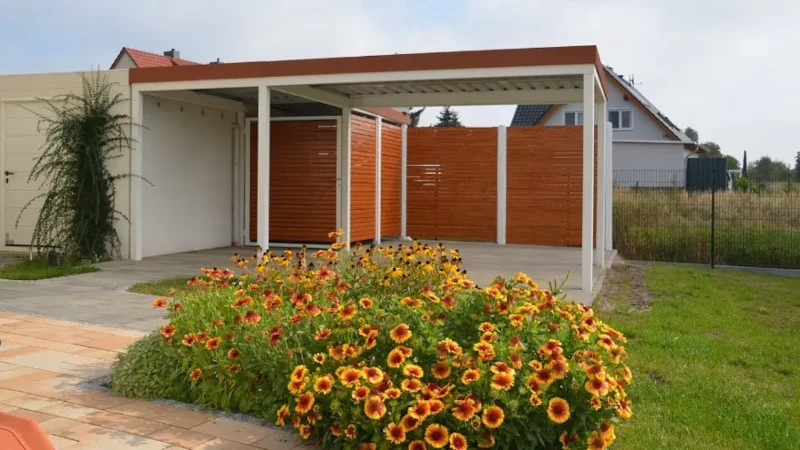 Modernes Carport mit Holzverkleidung und blühendem Garten im Vorgarten eines Hauses.